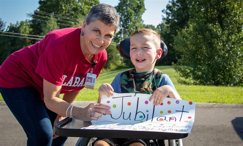 A teacher aide and a boy in a wheelchair wearing the word jubilant